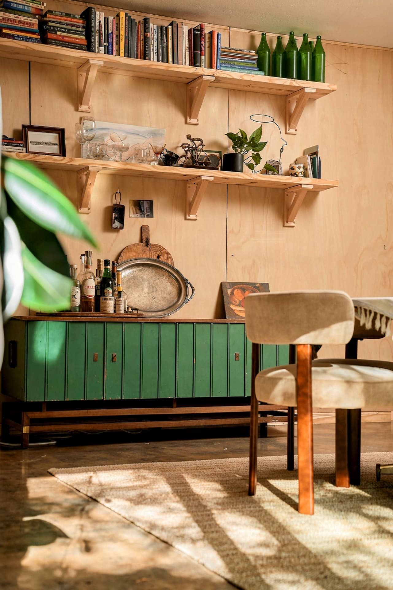 Sunlit bar cabinet with green doors and bottle shelves