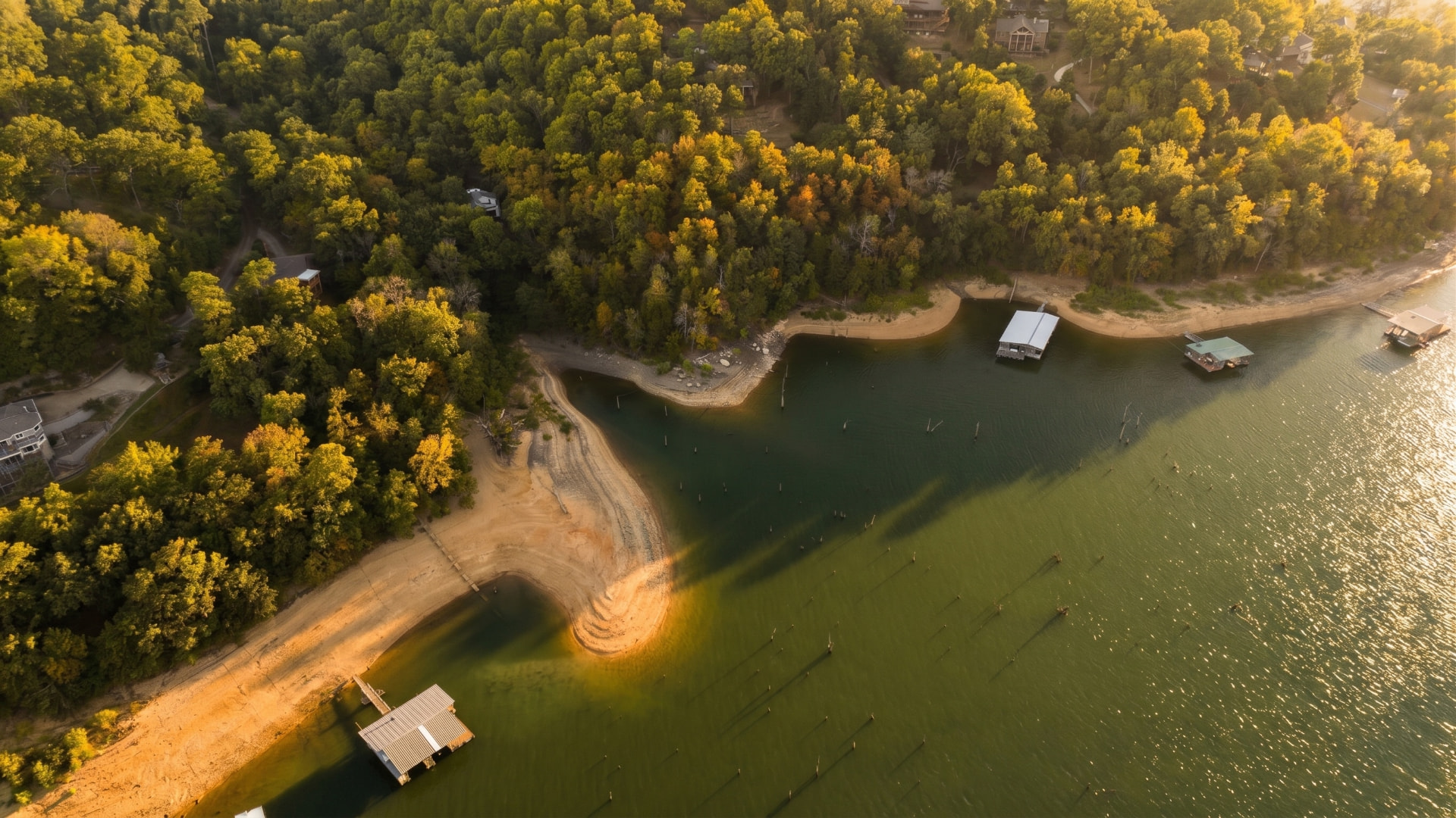 Aerial view of a peaceful lake shoreline at sunset with small docks near a golden forest
